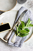 This image captures a beautifully arranged summer table setting centered around a mint theme Fresh mint leaves adorn the scene, complemented by vintage silverware, a rustic name tag, and ceramic plates