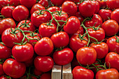 Close-up view of ripe red tomatoes with fresh green stalks, neatly arranged in a wooden crate at a vegetable stall