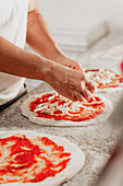 An anonymous chef prepares pizza dough with sauce and cheese in a pizzeria