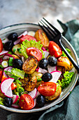 A vibrant bowl of Mediterranean salad, featuring roasted potatoes, plump olives, cherry tomatoes, crisp spring onions, lettuce, and sliced radishes, embodying spring freshness