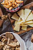 A rustic spread featuring slices of gourmet cheese alongside crispy breadsticks and biscotti, arranged on a wooden serving tray