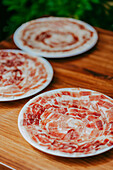 Freshly sliced Iberian Ham arranged on plates for cooking, displayed on a wooden table