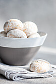 A close-up of powdered gingerbread cookies nestled in a modern ceramic bowl, presented on a soft fabric surface with a neutral backdrop