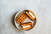 Fresh homemade waffles filled with fluffy vanilla marshmallow, served on a ceramic plate, top view on a textured background