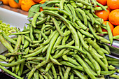 Fresh green beans piled at a market, with a background of vibrant oranges