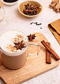 From above, A steaming mug of chai latte topped with star anise and sprinkled with cinnamon on a wooden board, in a rustic style