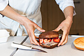 Crop unrecognizable baker holding sweet vegan sponge cake with whipped cream and strawberries in bakery