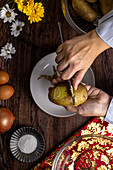 Top view of cropped unrecognizable person slicing a cooked potato on a plate in a rustic kitchen setup for a homemade meal, showcasing culinary preparation from above.