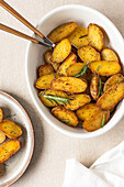 A top view image of seasoned roasted potatoes garnished with rosemary in a white ceramic bowl.