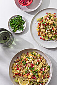 Top view of two bowls of colorful quinoa salad garnished with pomegranate seeds, nuts, and herbs.