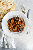 A hearty vegetable stew featuring eggplant, tomato, potato, bell pepper, onion, garlic, and basil, paired with flat bread on a white plate, perfect for a nutritious meal