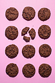 Top view of multiple chocolate chip cookies symmetrically placed on a bright pink surface, one is broken. The image captures the crunchy texture and delicious appeal of these freshly baked treats