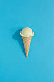 A vibrant Cream ice cream scoop sits atop a classic waffle cone against a blue background, casting a playful shadow