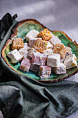 An assortment of colorful traditional Turkish delights presented on a ceramic plate, accompanied by black tea in a glass, and a vase of white roses adding to the elegant setup