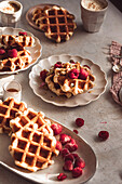 Frisch gebackene, hausgemachte Waffeln mit reifen Himbeeren und einem Spritzer Honig auf einem rustikalen Küchentisch