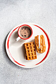 A plated breakfast of waffles with creamy vanilla marshmallow between them, paired with a cup of hot cocoa