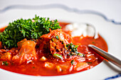 Close-up view of a bowl of hearty Ukrainian beetroot soup, known as borscht, garnished with parsley and a dollop of sour cream, ready to be enjoyed