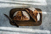 Sliced wholesome rye sourdough bread on a rustic wooden cutting board next to a serrated knife, with natural light casting shadows