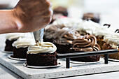 Unrecognizable crop baker squeezing cream from pastry bag on chocolate sponge cakes while preparing tasty vegan desserts in bakehouse