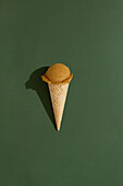 A vibrant coffee ice cream scoop sits atop a classic waffle cone against a green background, casting a playful shadow