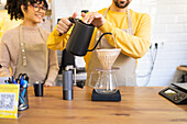 Barista carefully pours hot water into a coffee dripper over a carafe in a cozy cafe setting.