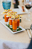 An artistic display of orange soup shooters topped with lavishly garnished crackers on an elegant dinner table setting