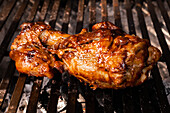 A chicken thigh with a rich glaze cooks on a grill, showcasing the juicy, caramelized texture typical of Mexican homemade food.