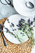 A charming summer table setting featuring white dinnerware, fresh lavender sprigs, and a ‘Thank you’ note, arranged on a woven placemat