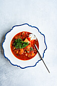 A top view of Ukrainian traditional beetroot soup served with a dollop of sour cream and garnished with parsley, presented on an ornate white and blue rimmed plate