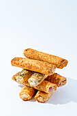 A variety of freshly baked puff pastry rolls, some topped with sesame and poppy seeds, arranged on a clean, white background.