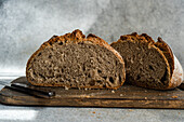 A freshly sliced loaf of homemade rye sourdough bread sits on a rustic wooden cutting board, showcasing its airy texture and crust