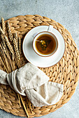 Top view of a cup of black tea accompanied by dry lemon pieces and a sugar-dusted homemade croissant on a woven placemat.