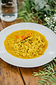 A vibrant plate of shrimp risotto, rich in color and flavor, sits invitingly on a rustic wooden table with a natural, floral backdrop