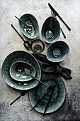 Top view of a luxurious table setting featuring emerald green ceramic plates, bowls, and dark cutlery on a textured grey surface.