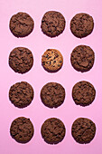 Flat lay photography of twelve double chocolate chip cookies arranged on a vibrant pink background