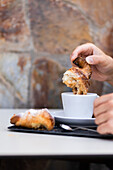 A cropped unrecognizable person enjoying a traditional breakfast of Colombian origin coffee and a freshly baked, homemade croissant with a dusting of powdered sugar.