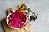 A vibrant bowl of fermented cabbage with slices of beetroot, spicy red pepper, and garlic, on a wooden board with olive oil and spices.