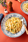 Von oben: Hausgemachte italienische Pasta mit Petersilie und Parmesan auf rotem Hintergrund neben einer Pfeffermühle, einer Käsereibe und Salz