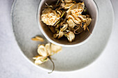 A close-up shot of withered roses in muted tones, placed in a simplistic gray ceramic bowl, conveying a theme of decay and nostalgia