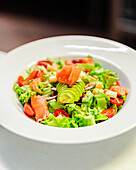 A vibrant house salad featuring fresh mezclum, succulent salmon slices, ripe cherry tomatoes, crisp onion, juicy apple, and creamy avocado served in a white bowl.