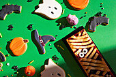 A vibrant set of homemade Halloween cookies, with designs such as ghosts, bats, pumpkins and witch hats, arranged on a lively green background