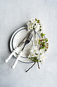 Elegant table setting with white cherry blossoms on a stack of plates with silverware beside