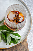 Top view of a crystal glass holding a cherry cocktail garnished with ice, mint leaves, and a star anise, presented on a plate.