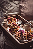 A warm and inviting breakfast scene featuring freshly baked waffles with raspberries, accompanied by coffee and juice, served on a wooden tray in bed