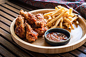 Crispy fried chicken hips served alongside golden french fries and a bowl of rich BBQ sauce, presented on a wooden plate with a rustic backdrop.