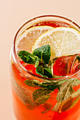 Vibrant berry-orange lemonade garnished with fresh mint leaves and lemon slices, served in a glass with ice; perfect for a hot day.