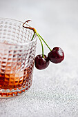 A close-up image of a glass filled with gourmet cherry liqueur, accompanied by ripe cherries draping gracefully over the rim