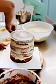 An unfinished cake being layered with creamy frosting beside a mixing bowl and kitchen mixer in the background