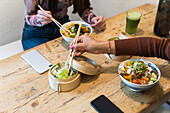 From above of crop anonymous female eating delicious poke dish with chopsticks while sitting at wooden table in restaurant