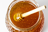 From above closeup of dipper stirring fresh aromatic golden honey in glass jar